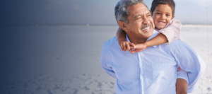 Older man carrying small child on back walking on beach